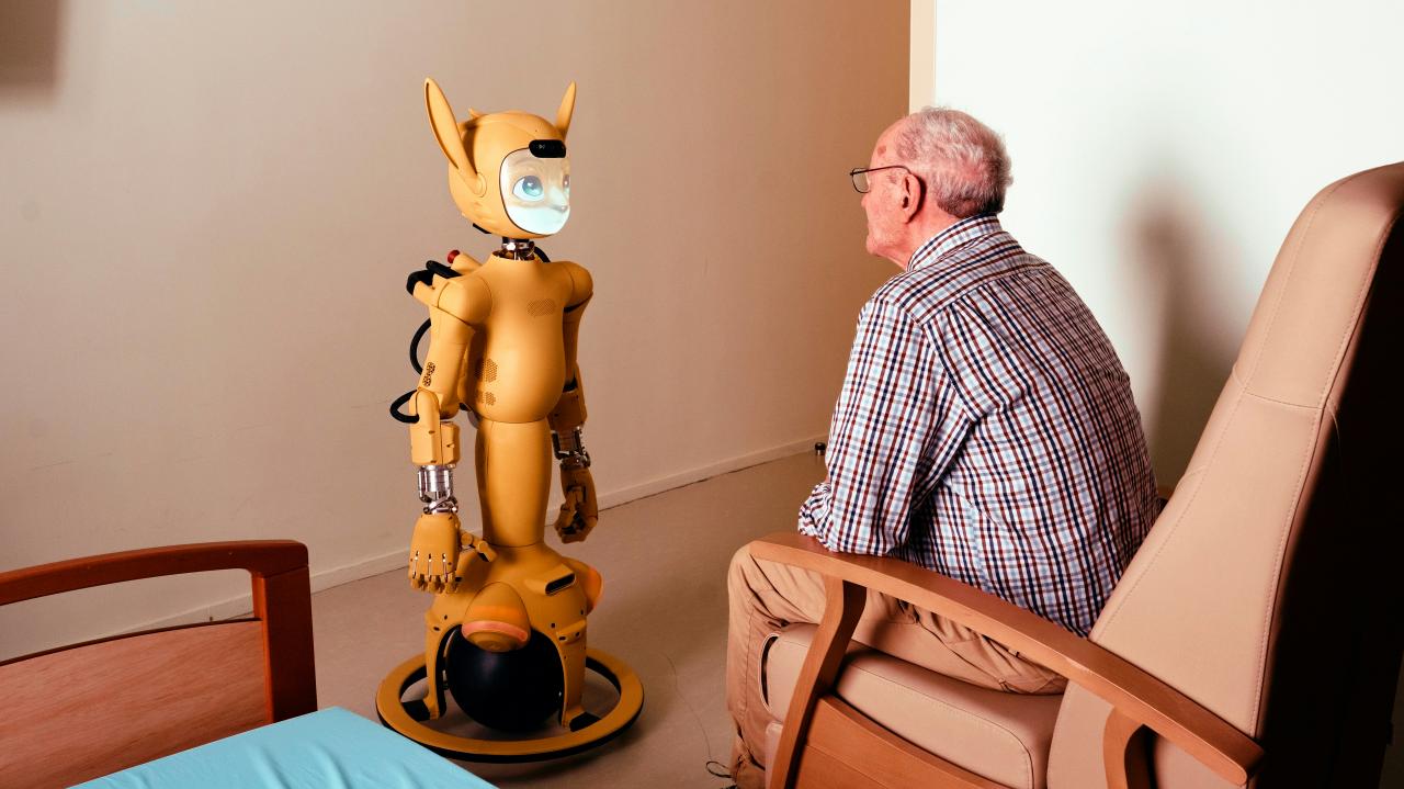 Elderly man converses with a yellow robot.