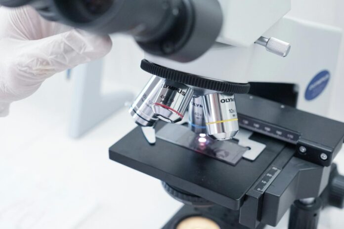A person in white gloves is looking through a microscope